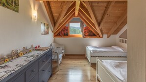 Een slaapkamer met een schuine balkenkap, houten balken, een raam met uitzicht op bomen, een dressoir, twee bedden en een stoel.