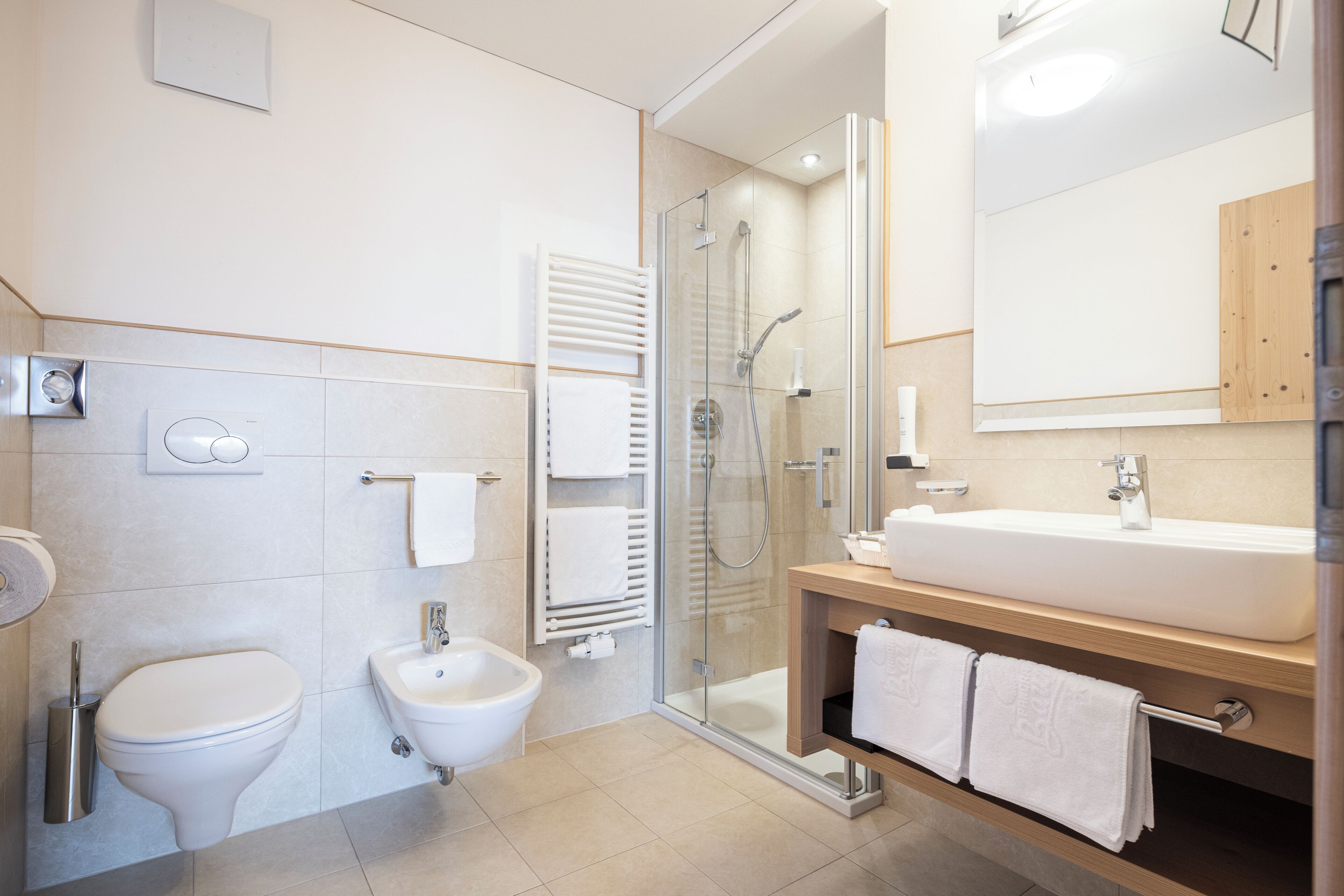 Et moderne badeværelse med et glasvæg-afskærmet brusebad, en hvid vask og et toiletbidét.