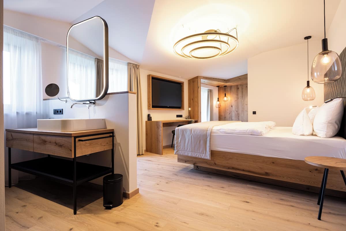 A modern bedroom with a wooden bed, a bedside table, a built-in desk, a large mirror, and a TV.