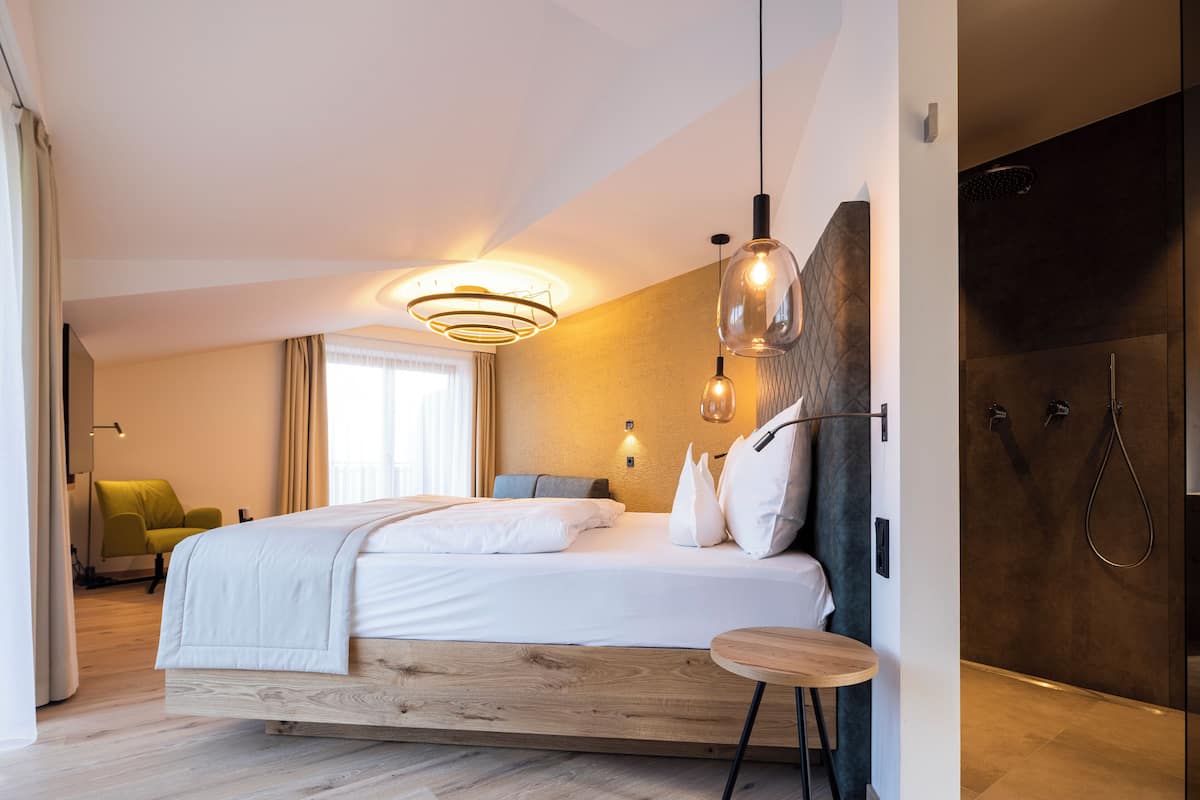 A modern hotel room with a wooden bed, a small round table, a shower, and a green chair.