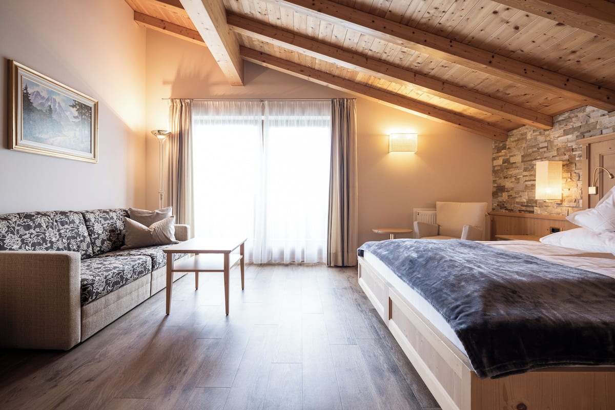 A bedroom with a wooden ceiling, a bed, a sofa, a table, and a window with curtains.