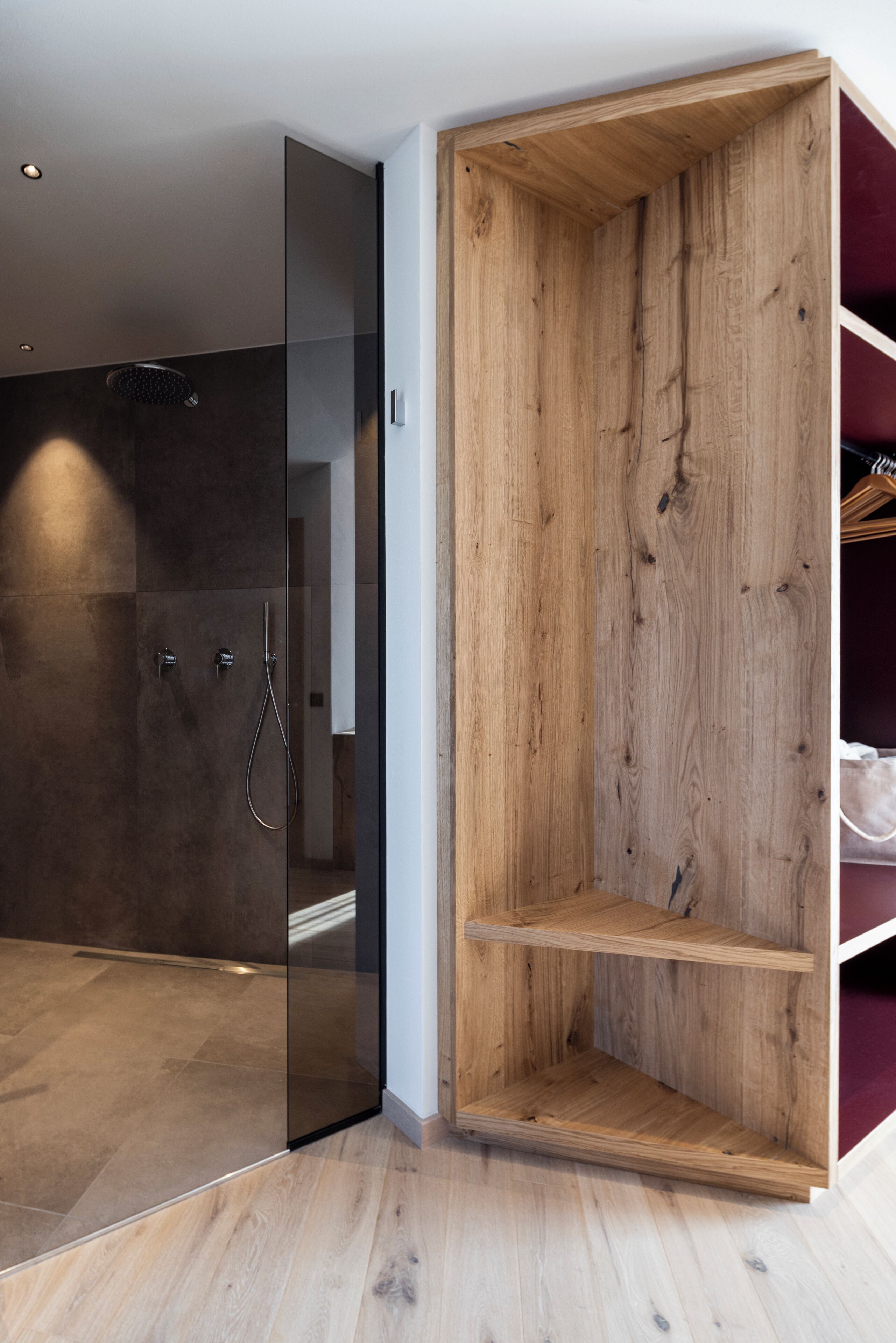 Un baño moderno con cabina de ducha de vidrio, estanterías de madera y suelo de baldosas.