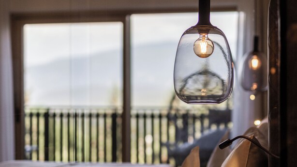 A bedroom with a bed, pillows, and a hanging light fixture. - Hotel Baumwirt (Castelrotto)
