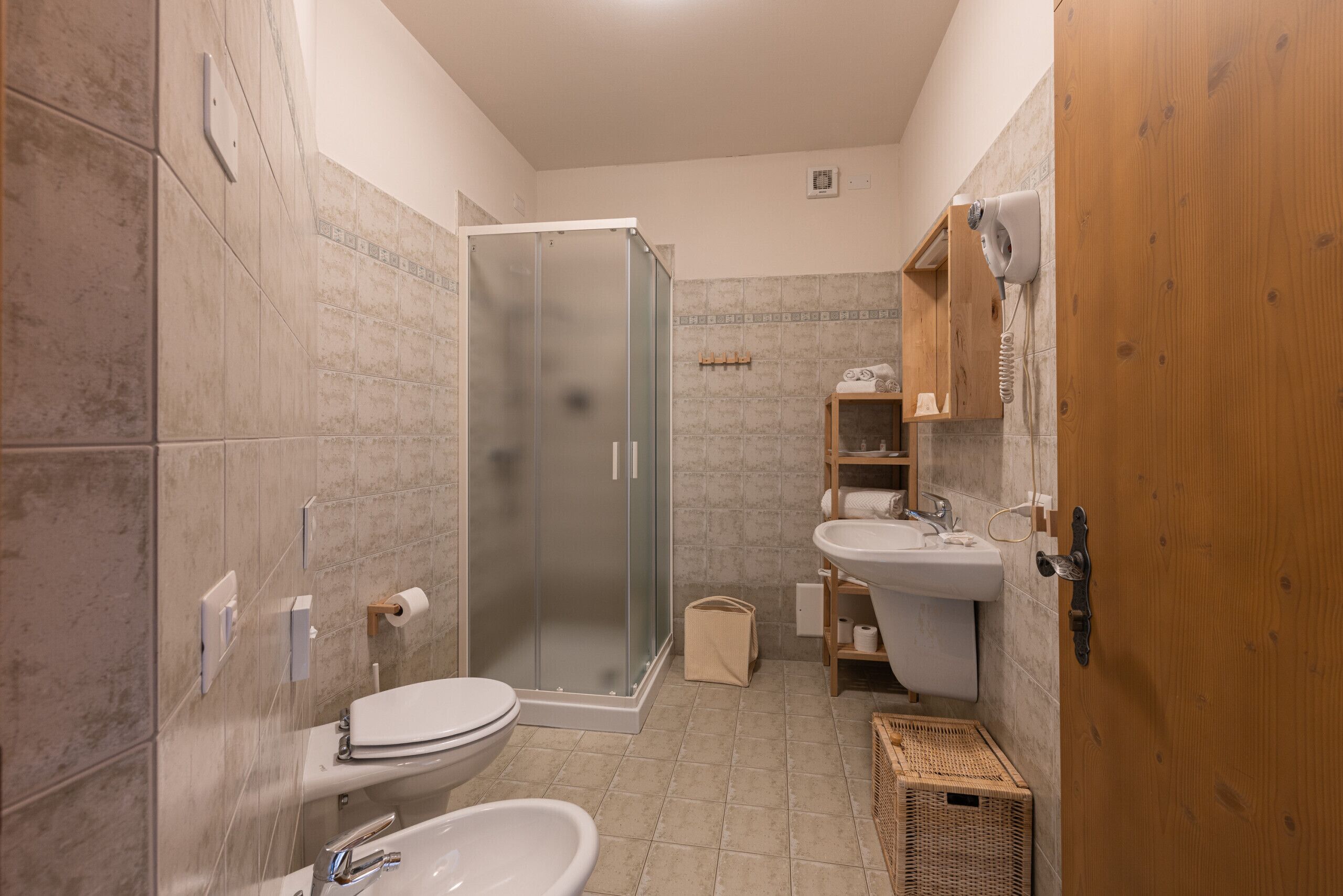 Ein Badezimmer mit Dusche, Toilette, Waschbecken und Holzregalen.