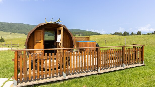 A wooden cabin with a porch and a fence, set in a grassy field with hills in the background. - Agriturismo Filippon- Room Stalla (Tambre)