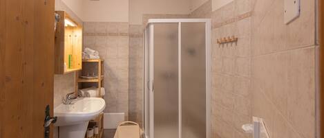 A bathroom with a wooden door, a white sink, a glass-enclosed shower, and beige tiled walls.