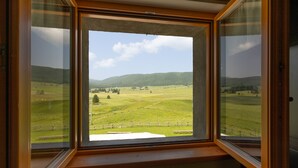 Ein Zimmer mit großem Fenster und Blick auf eine grüne Landschaft mit Hügeln und blauem Himmel.