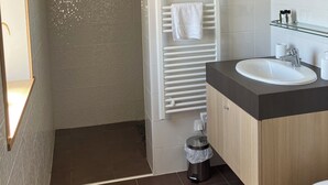 Une salle de bain moderne avec une douche blanche, une douche à l’italienne entourée de parois de verre, une serviette blanche suspendue à un porte-serviettes, un lavabo avec un plan de toilette foncé et des toilettes.