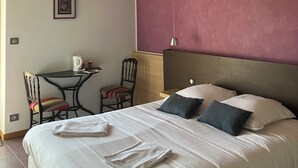 Une chambre d’hôtel avec un grand lit, une petite table avec des chaises, une lampe fixée au mur et un tableau encadré accroché au mur.