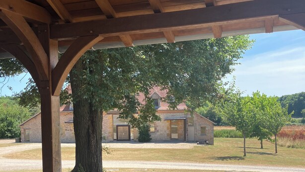 Une terrasse en bois avec un banc et une table, un arbre et un bâtiment en arrière-plan.