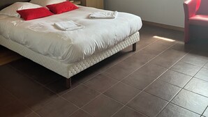 Une chambre d’hôtel avec un lit, une armoire en bois, une chaise rouge et une fenêtre laissant entrer la lumière du soleil.
