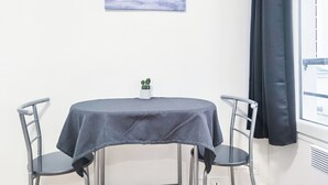 Una mesita redonda con mantel gris, dos sillas grises, una pequeña planta en maceta y un cuadro de un mar tranquilo en la pared.