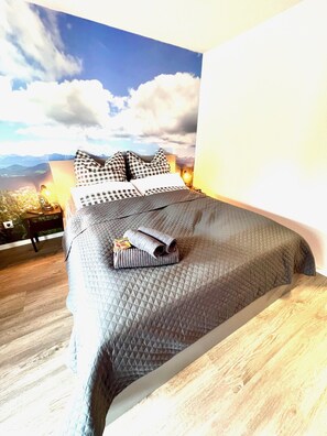A bedroom with a bed, pillows, a rolled towel, and a nightstand with a lamp.