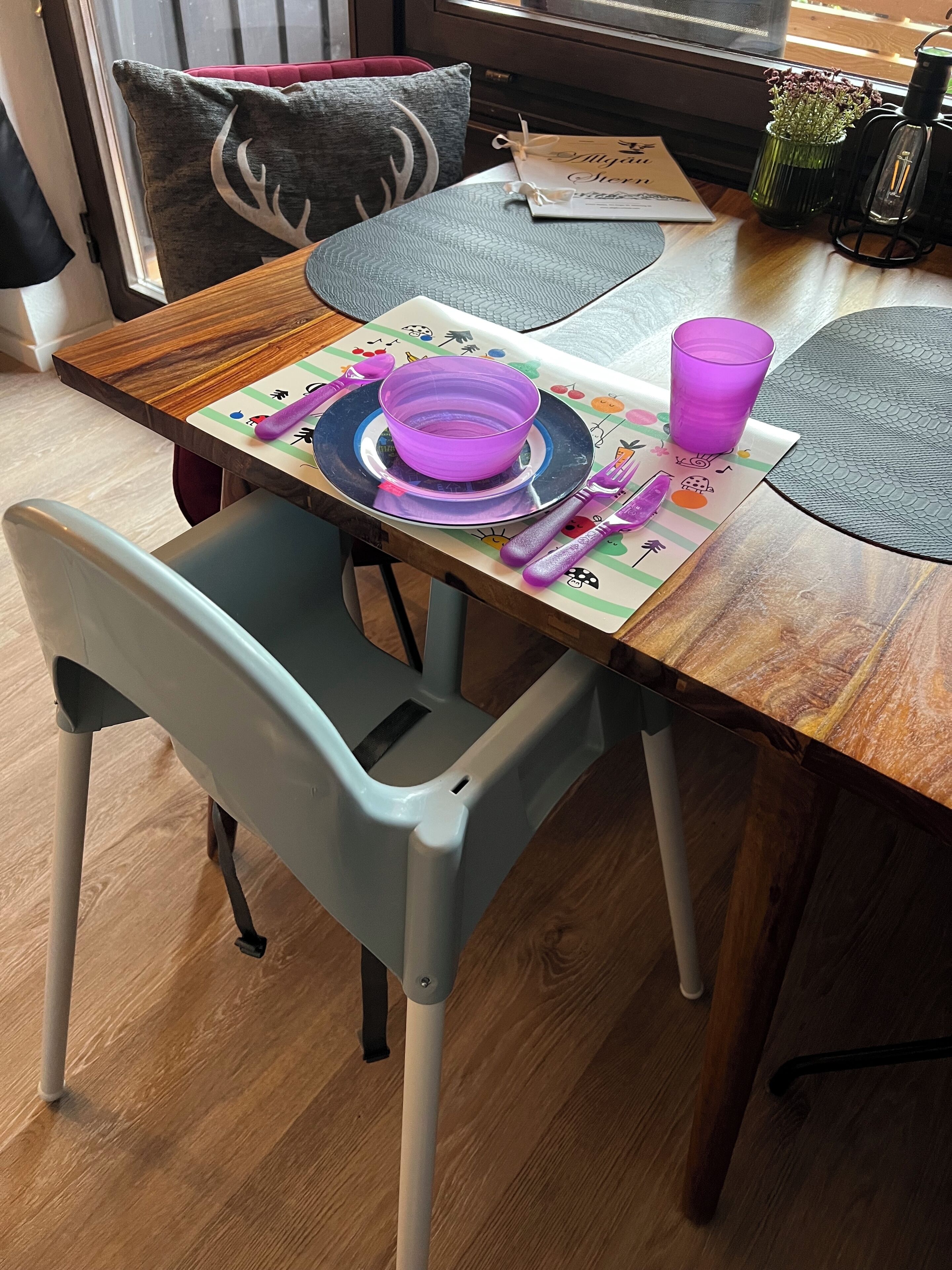 Una mesa de comedor con un tazón morado, platos y cubiertos. Hay una silla frente a la mesa.