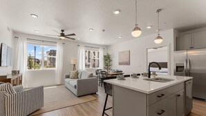 Une cuisine moderne dotée d’un grand îlot central, un coin repas avec une table et des chaises, et un salon avec un canapé et un fauteuil à rayures.