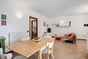 A dining area with a wooden table and chairs, a bowl of cereal, a radiator, a television on a cabinet, a sofa, and a small cart.