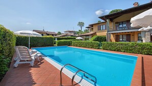A swimming pool with a metal ladder, lounge chairs, and umbrellas.
