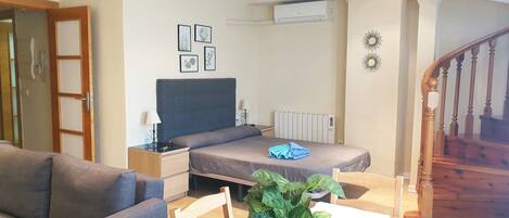 A bedroom with a bed, bedside table, lamp, and a radiator. There is a staircase to the right and a door to the left.