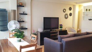 A living room with a TV, sofa, dining table, chairs, and decorative items. - Rooms San Marcos (Madrid)