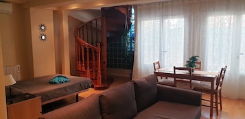 Ein gemütliches Zimmer mit einem Bett, einer Couch, einem Esstisch mit Stühlen und einer Treppe.