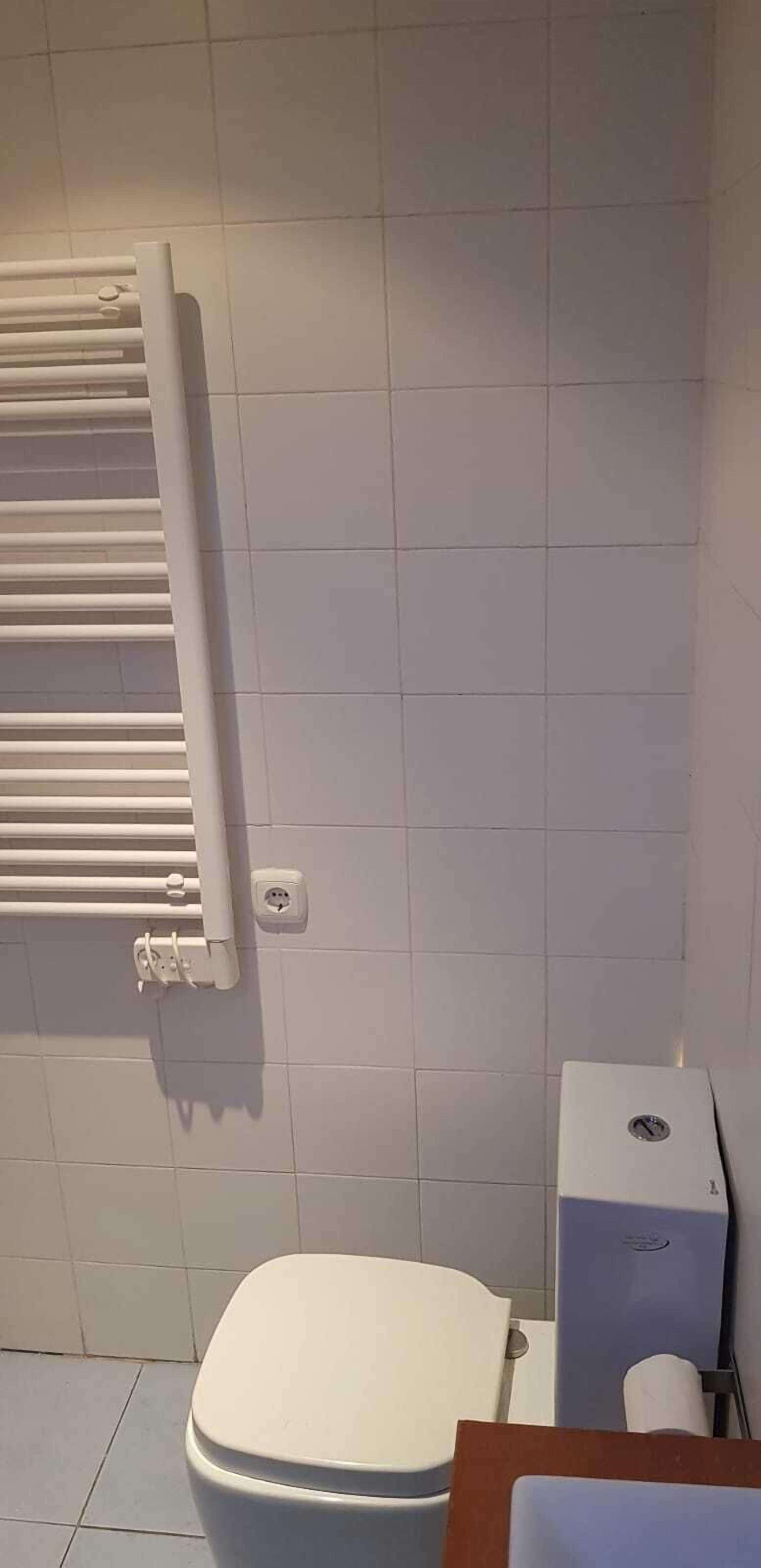 A bathroom with a toilet, a white radiator, and a paper towel dispenser.