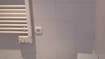 A bathroom with a toilet, a white radiator, and a paper towel dispenser.