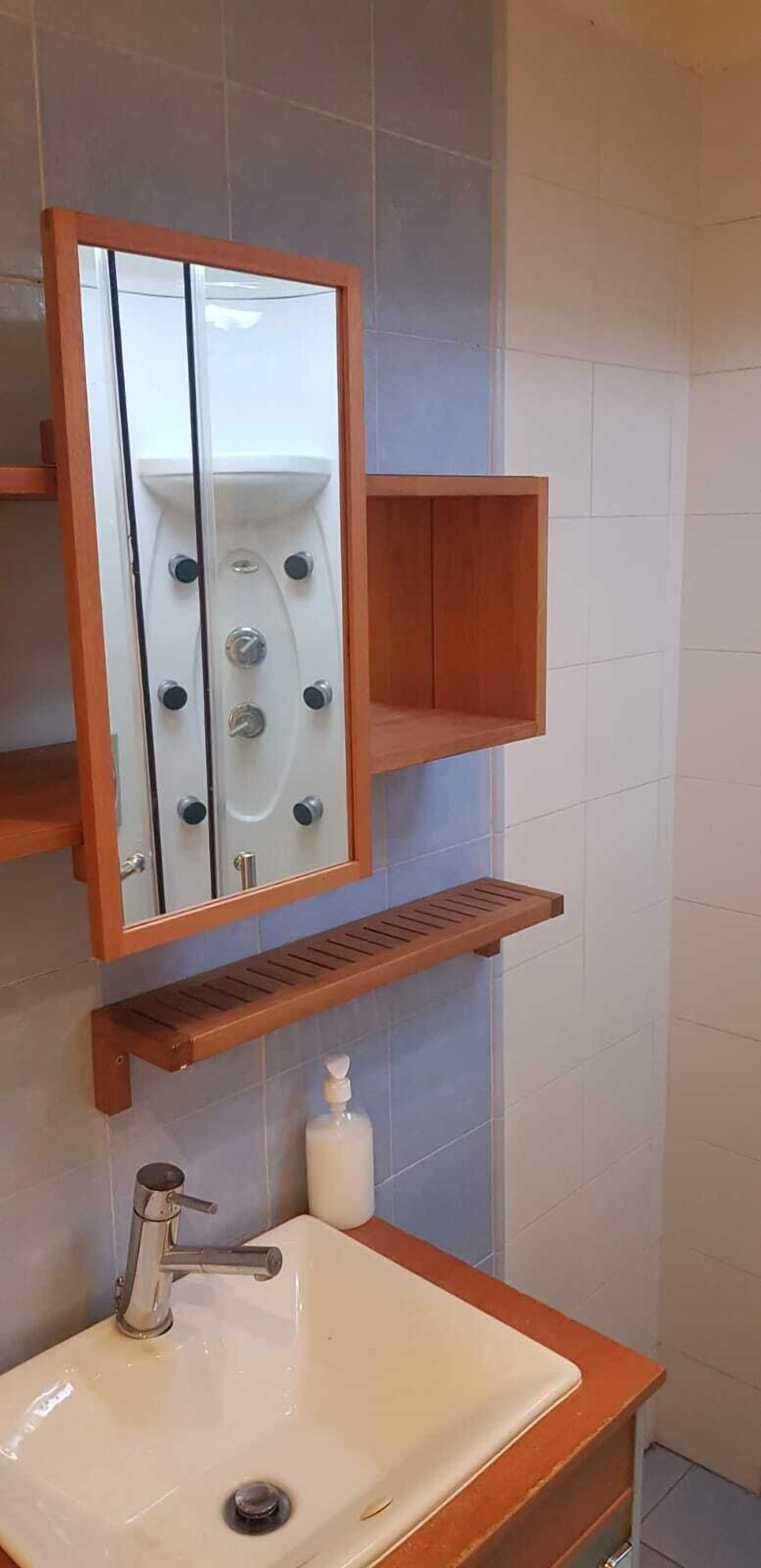 A bathroom with a white sink, a mirror, and a wooden shelf.