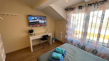 A bedroom with a bed, a desk, a chair, a TV, and a window with curtains.