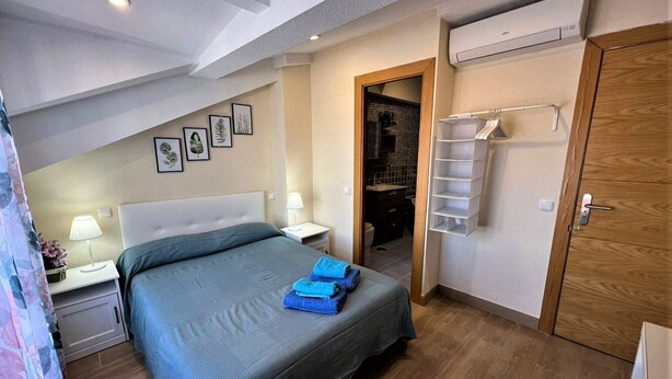 A bedroom with a bed, nightstands, a wardrobe, an air conditioning unit, and a bathroom visible through an open door. - Rooms San Marcos (Madrid)