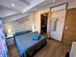 Ein Schlafzimmer mit Bett, Nachttischen, einem Kleiderschrank, einer Klimaanlage und einem durch eine offene Tür einsehbaren Badezimmer.