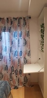 Ein Zimmer mit einem blumigen Vorhang, einem weißen Schreibtisch und einer Pflanze an der Wand.