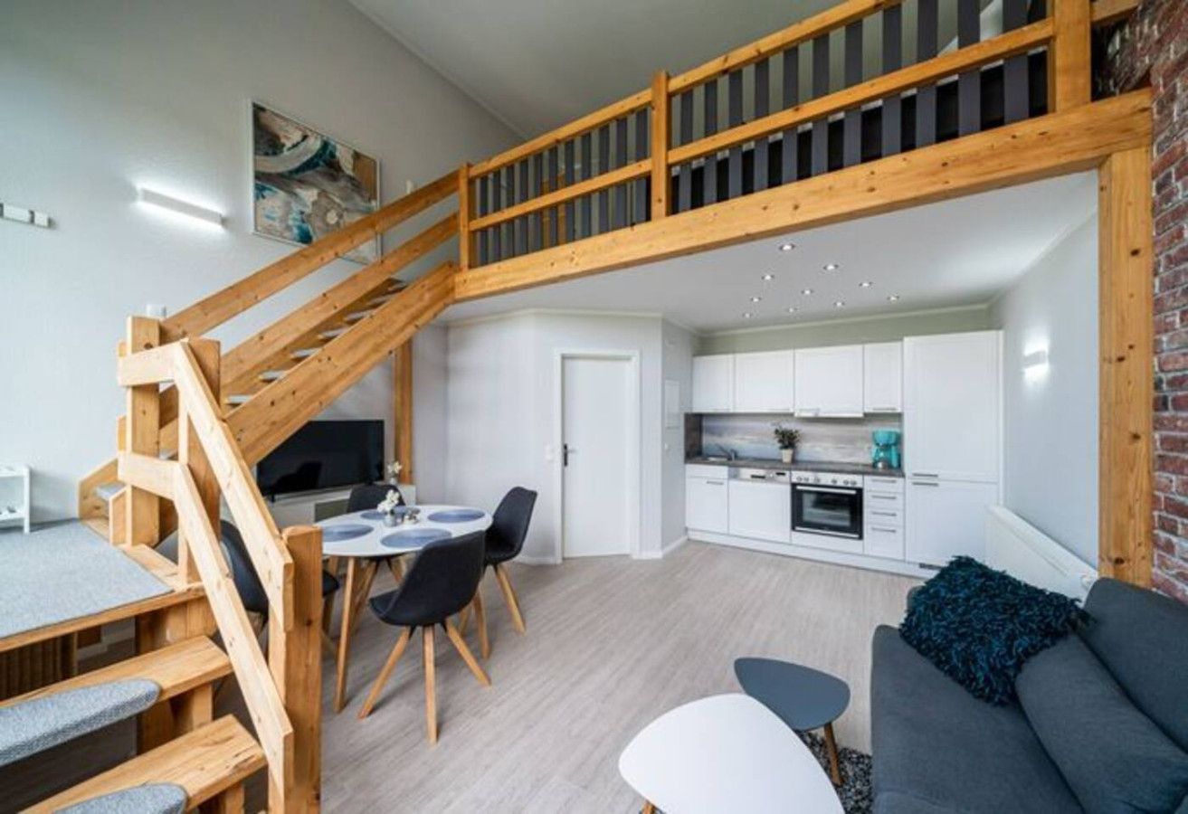 A modern interior with a wooden staircase, a dining area, a kitchen, and a living room.