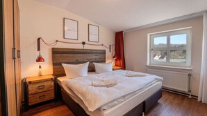 A neatly made bed with white linens, a wooden headboard, and a nightstand with a lamp. - Inselzeit Comfort Suite No. 21 (Sellin)