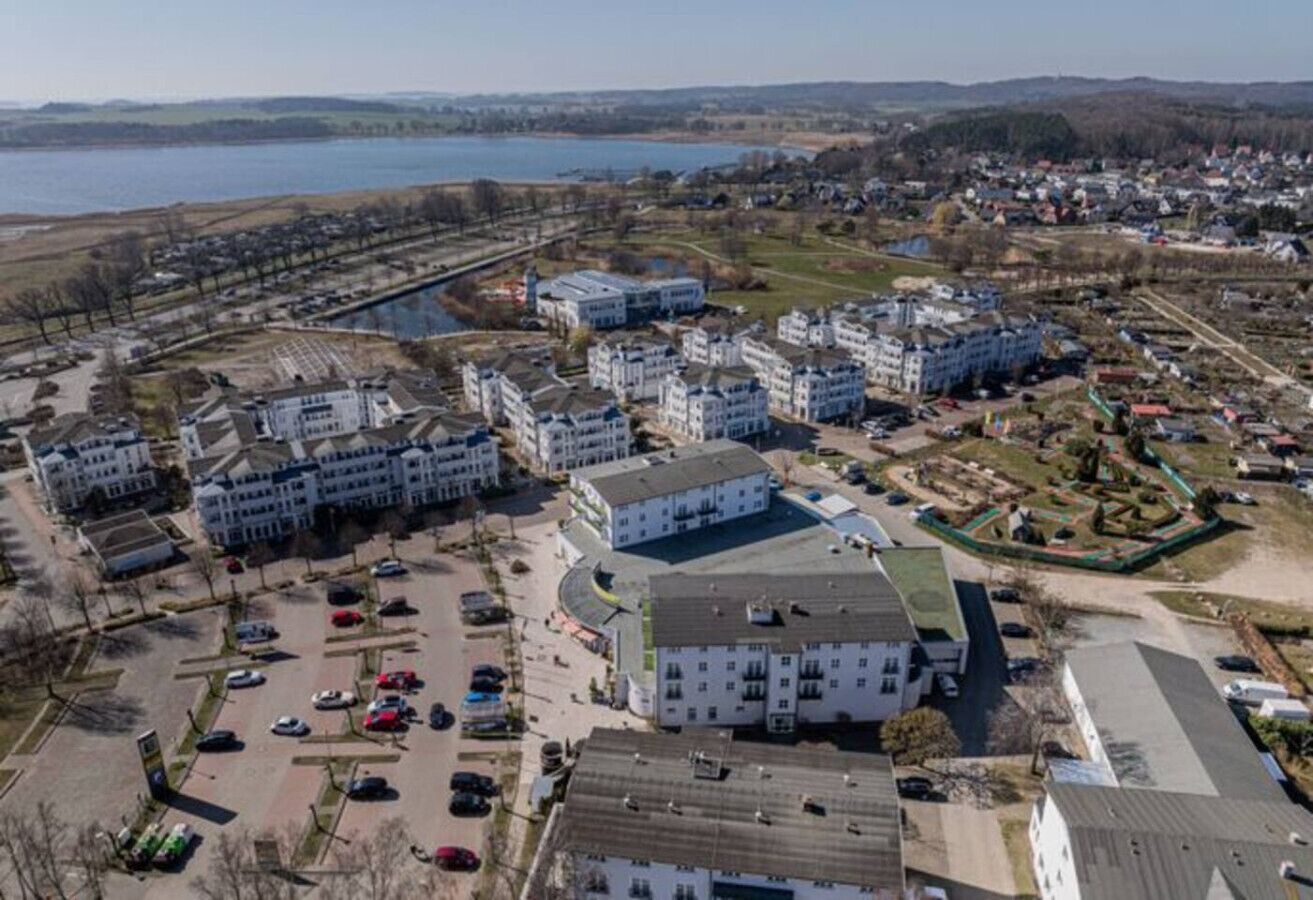 Vista aérea de uma área residencial com vários edifícios de apartamentos, um estacionamento e um corpo d'água ao fundo.