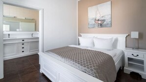 Une chambre à coucher avec un lit, des tables de chevet, un tableau et une salle de bain visible à travers une porte ouverte.