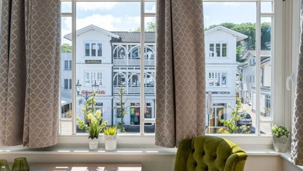 A room with a large window, a green chair, and a table with a vase of flowers. - Villa Meeresgold `Strandidyll` Premium Suite (Binz)