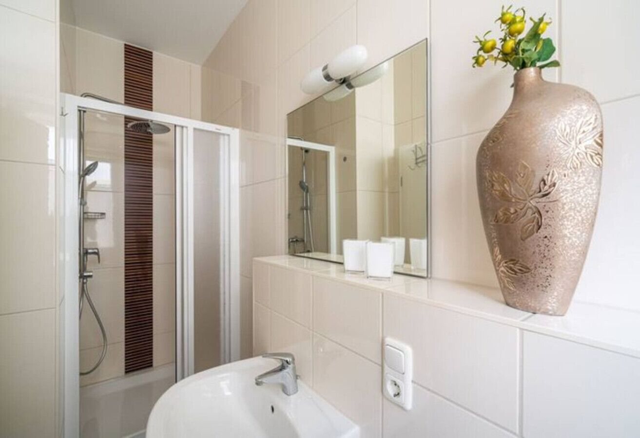Une salle de bain moderne avec une douche à parois de verre, un lavabo blanc et un grand vase décoratif accroché au mur.