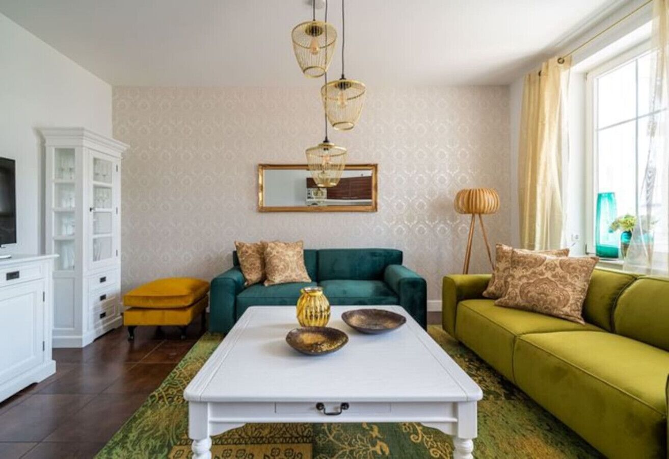 A living room with a white coffee table, green sofas, and a yellow ottoman.