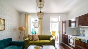 A modern living room with a green sofa, a white coffee table with decorative items, and a kitchen with wooden cabinets and a built-in oven. - Villa Meeresgold `Strandidyll` Premium Suite (Binz)