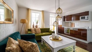 A living room with a green sofa, a white coffee table, and a kitchen area with wooden cabinets and a microwave. - Villa Meeresgold "Sea View" Premium Suite (Binz)