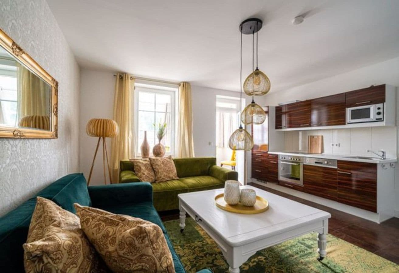 A living room with a sofa, a coffee table, and a kitchen area with cabinets and appliances.