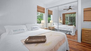 Une chambre moderne avec un grand lit, un ventilateur de plafond et un grand miroir qui reflète la pièce.