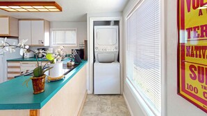 A compact kitchen with a built-in washer and dryer, a teal countertop, and a small potted orchid.