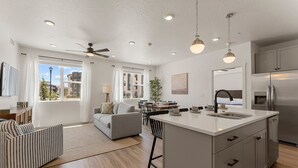 A spacious living area with a large window, a dining table, and a kitchen with a central island. - Comfort At Cliff Side 2 Bedroom Condo (Hurricane)