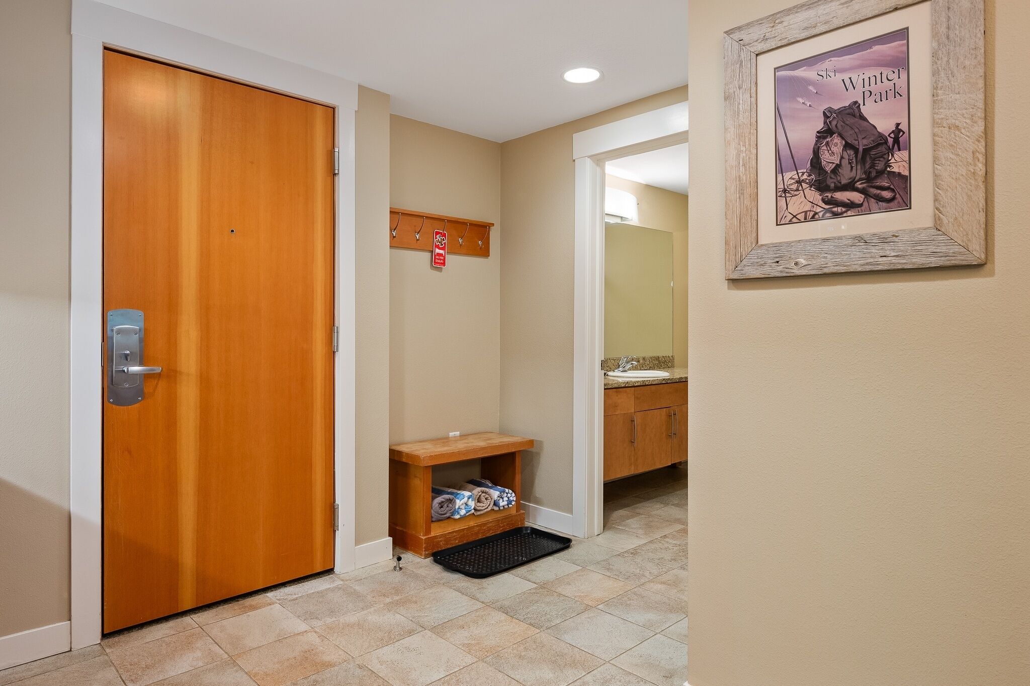 A hallway with a wooden door, a coat rack, a framed picture, and a small shelf with towels.