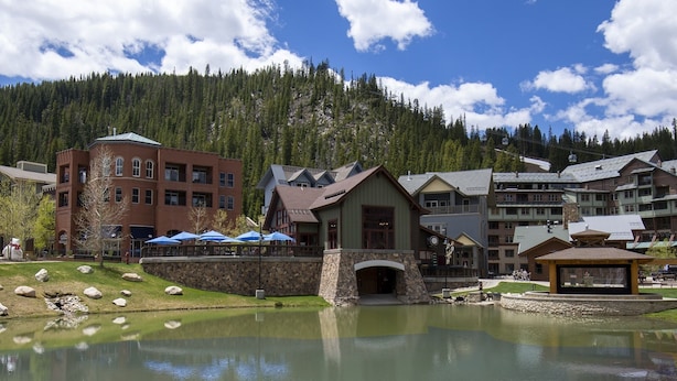 A lakeside hotel with a stone bridge, a pond, and a mountain backdrop. - Fraser Crossing 1 Bedroom Cabin (Winter Park)