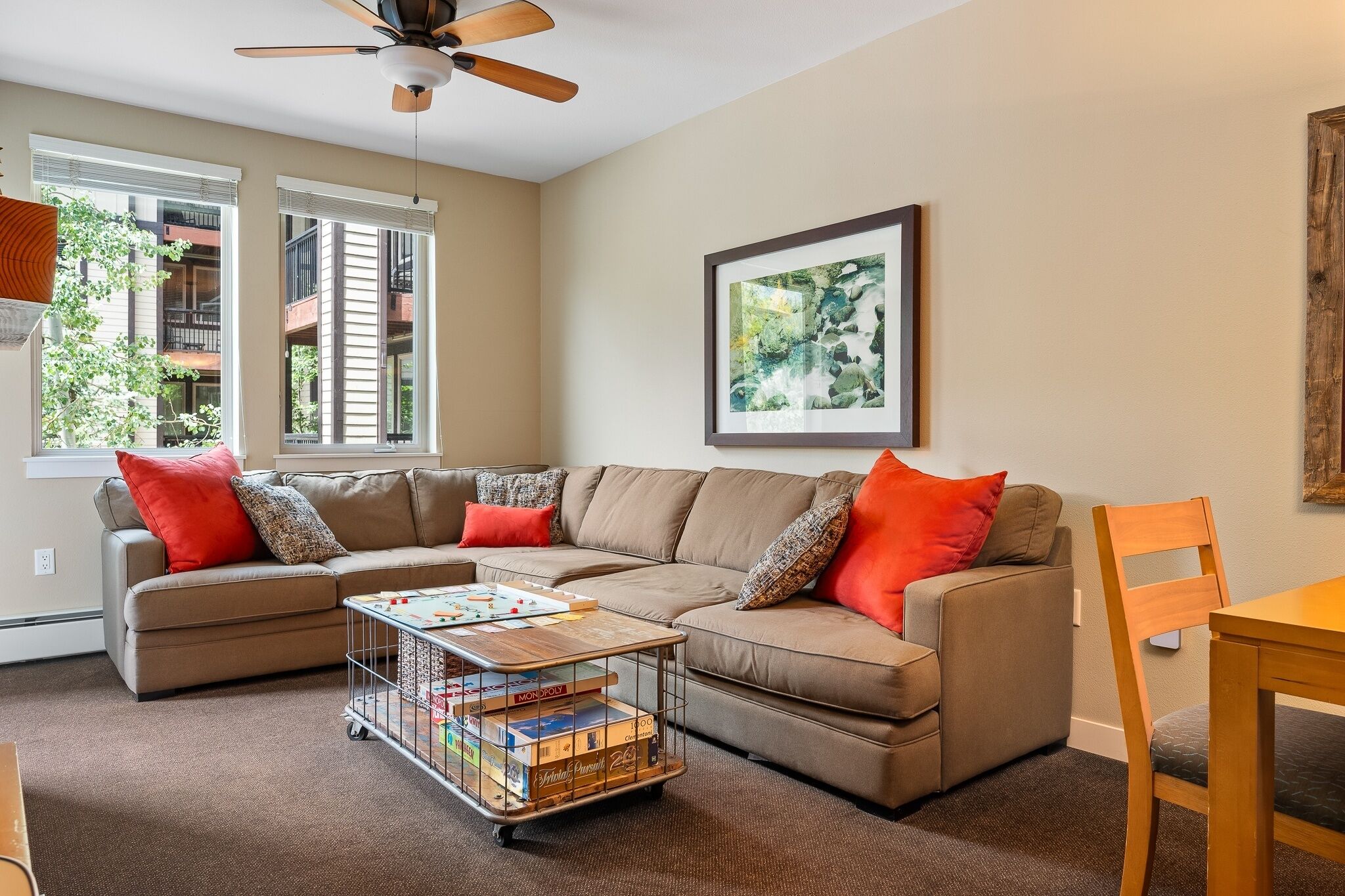 A living room with a sectional sofa, a coffee table with board games, a ceiling fan, and a framed picture on the wall.