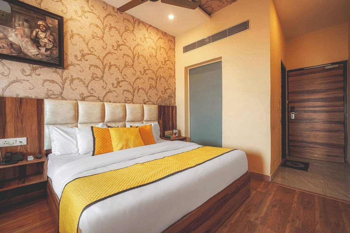 Une chambre d’hôtel avec un grand lit, une tête de lit agrémentée de plusieurs coussins, une table de chevet avec un téléphone et une porte avec un panneau en bois.
