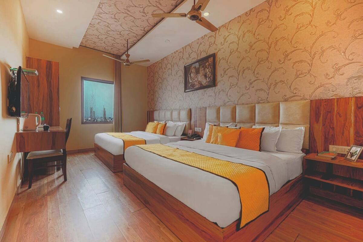 Une chambre d’hôtel avec un grand lit, deux tables de chevet, un bureau avec une chaise, une fenêtre donnant sur la ville et un ventilateur de plafond.