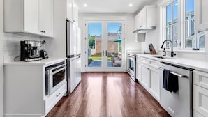 A modern kitchen with white cabinetry, a built-in oven, a coffee maker, and a window overlooking a backyard.